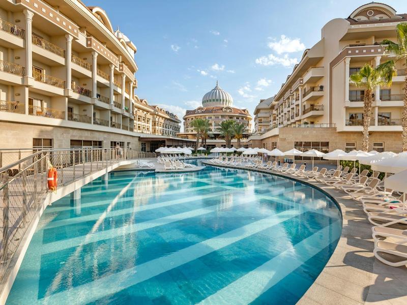 Gran piscina al aire libre entre edificios de hotel con tumbonas y sombrillas bajo cielo despejado.