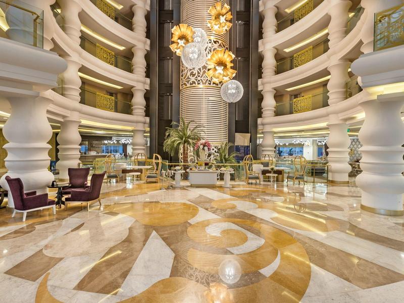 Gran vestíbulo de hotel con suelo de mármol, muebles elegantes y luces decorativas en el techo.