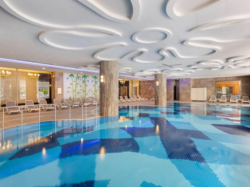 Piscina interior con techo elegante, columnas y zonas de descanso cómodas en un hotel.