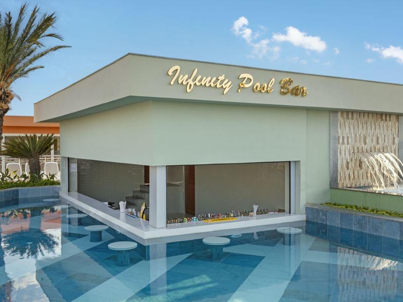 Bar de piscina moderna con asientos dentro del agua y letrero Infinity Pool Bar