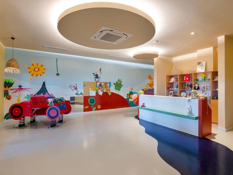 Sala de juegos infantil colorida en hotel con coche y murales alegres.