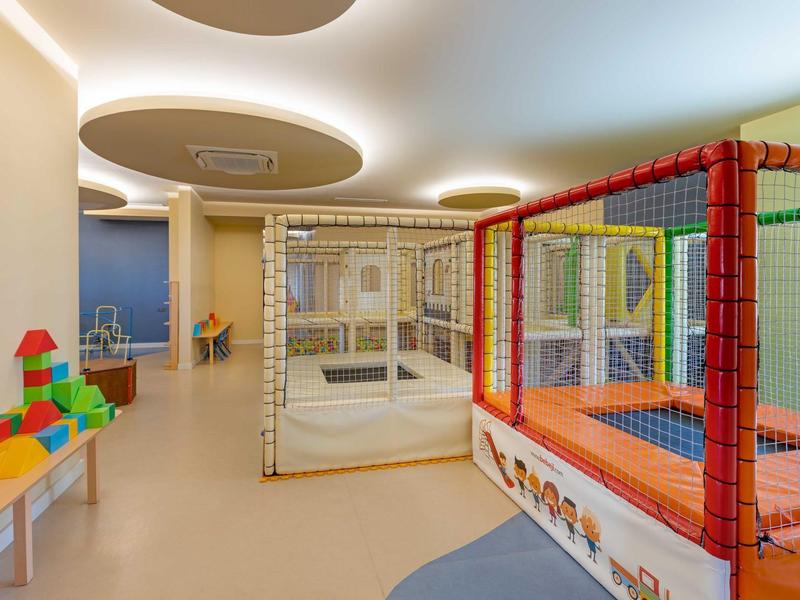 Vista interior de una moderna zona de juegos para niños en un hotel con trampolín colorido y bloques de construcción.