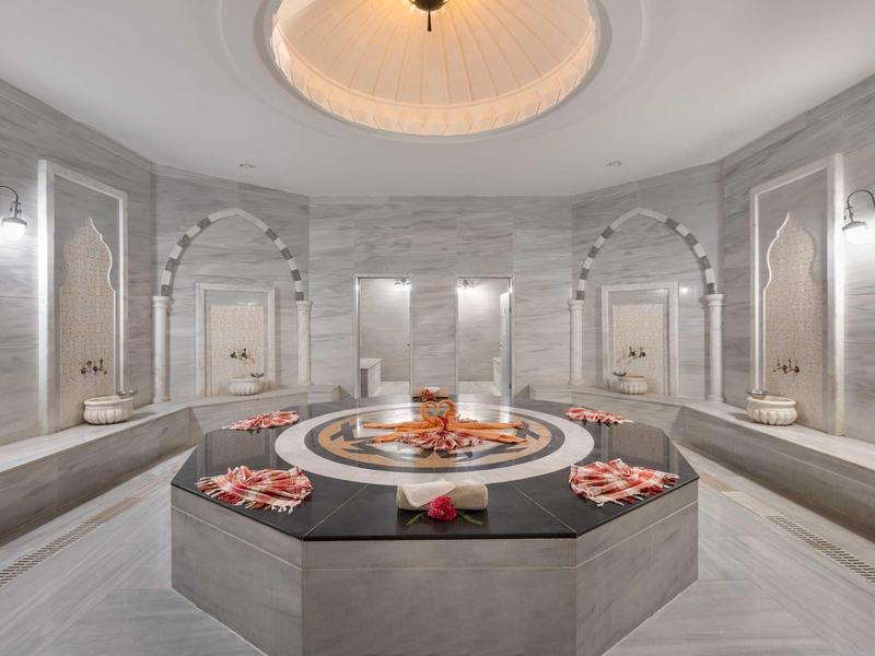 Hamam turco lujoso con piscina central y detalles decorativos en gris y blanco.