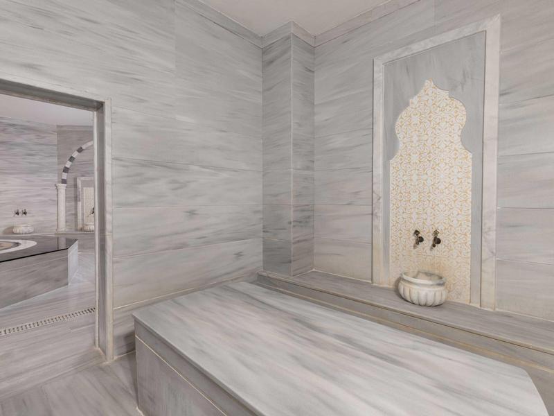 Hamam turco moderno con paredes de mármol, cama central y grifo de agua tradicional.