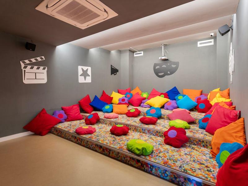 Acogedora sala de cine en casa con gran alfombra y cojines coloridos en el suelo.