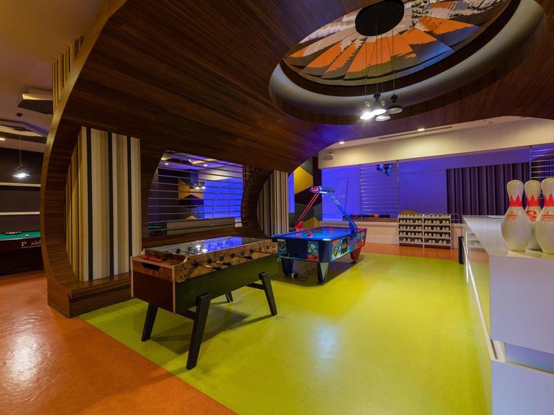 Zona de ocio con futbolín, mesa de billar y bolos en un interior colorido.