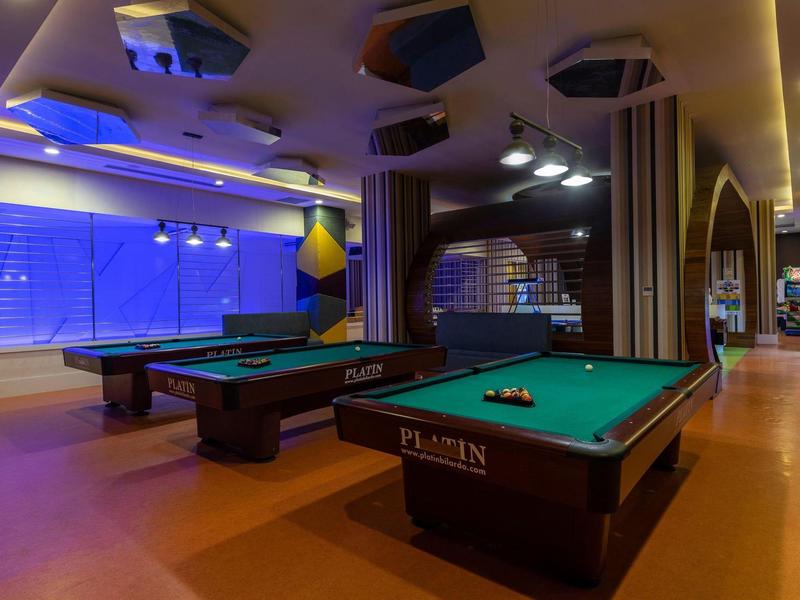 Salas modernas de billar con dos mesas verdes y luz tenue en un hotel.