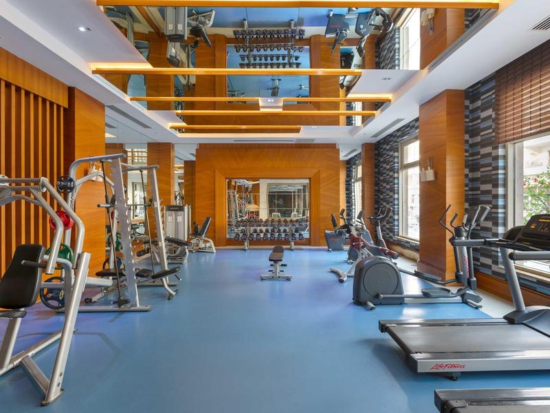 Sala de fitness bien iluminada con suelo azul y equipos modernos junto a grandes ventanas.