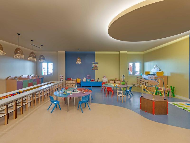 Sala de juegos para niños bien iluminada con muebles coloridos y áreas de juego variadas en un hotel.