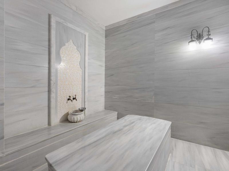 Hamam turco moderno con revestimiento de mármol y lavabo tradicional en la pared.