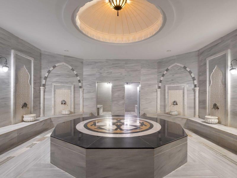 Sala de baño turca con iluminación suave, mármol gris y una fuente central octogonal.