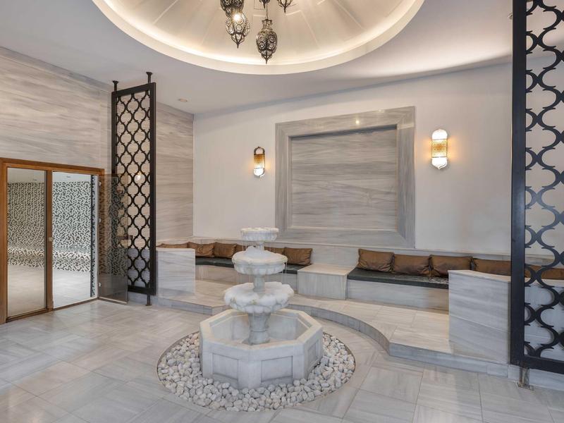 Lobby elegante de hotel con fuente de mármol, área de asientos y rejas metálicas decorativas.