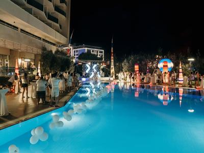 Busy hotel pool area at night with many people and lights