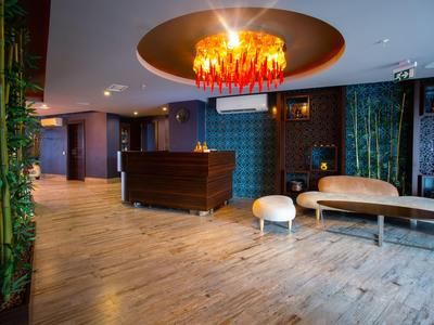 Hall d'hôtel moderne avec sol en bois, comptoir d'accueil élégant, coin salon stylé et un lustre remarquable.