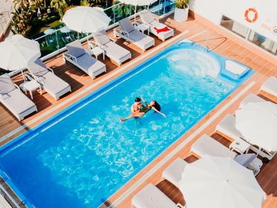 Modern pool area with sun loungers and umbrellas on a hotel rooftop terrace.