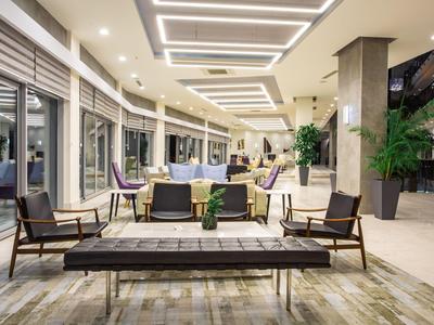 Espace lounge d'hôtel moderne avec bancs en bois, fauteuils et éclairage élégant.