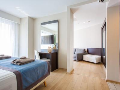 Helles Hotelzimmer mit Doppelbett, blauer Bettdecke, großem Spiegel und angrenzendem Wohnzimmerbereich.