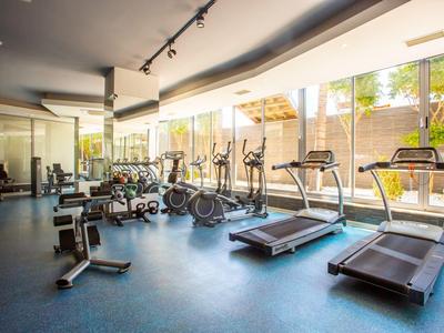 Helles Fitnessstudio mit cardio-Geräten, Hanteln und großen Fenstern mit Blick nach draußen.