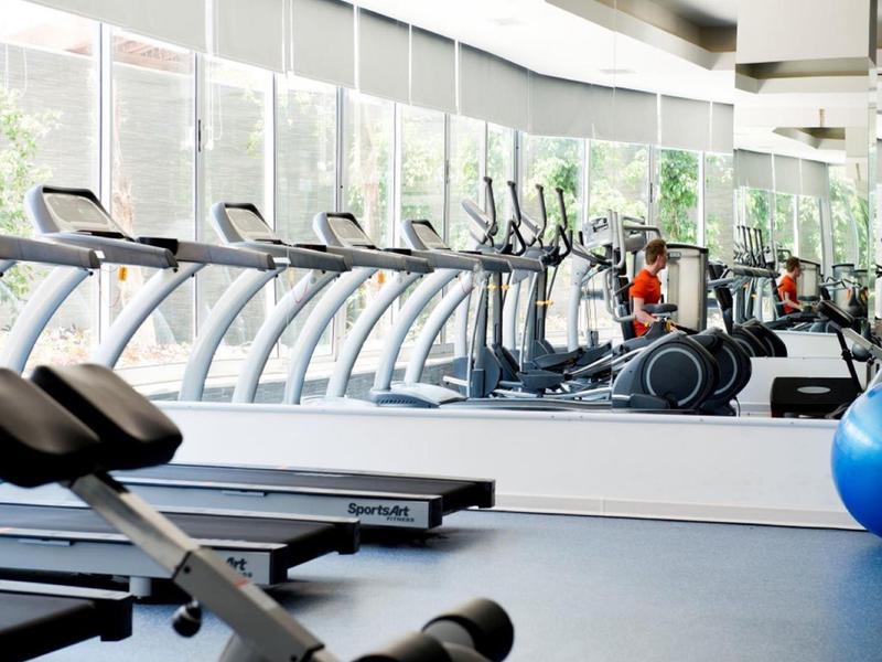 Bright gym with treadmills, exercise bikes, and large windows overlooking greenery.