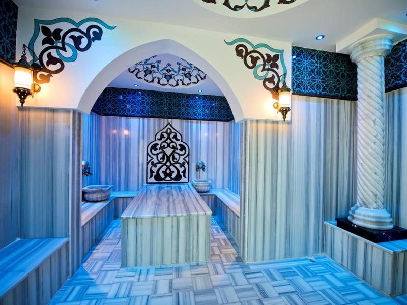 Luxurious hotel spa room with ornate decor, arched entrance, soft lighting and tiled flooring.