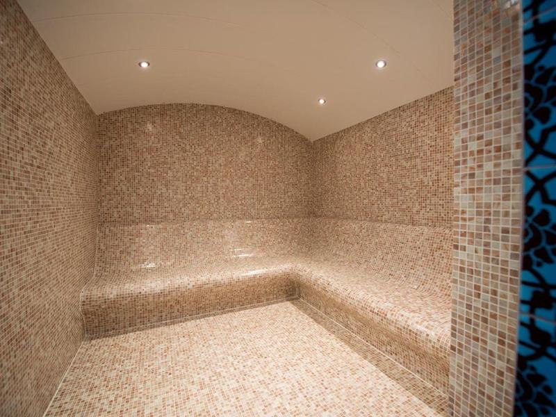 Modern steam room with beige mosaic tiles and built-in seating under recessed lights.