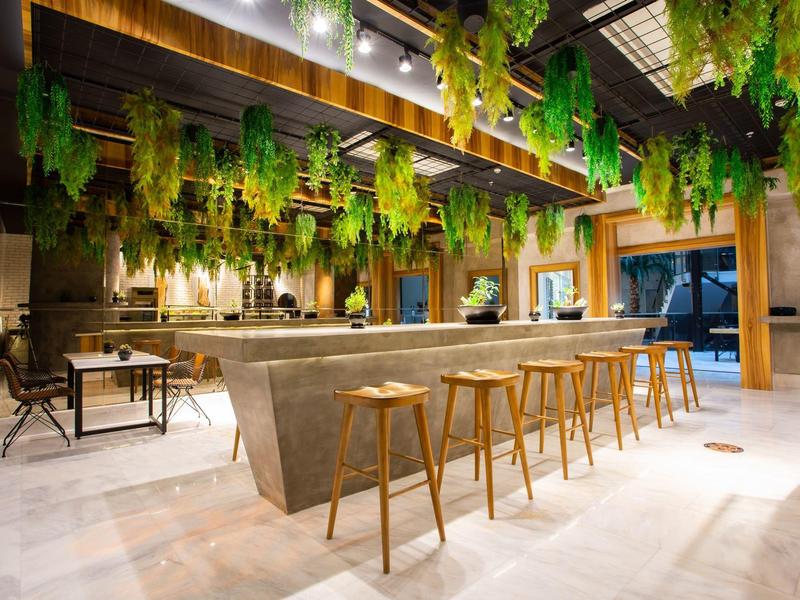 Modern hotel lobby with hanging plants, a long marble bar, and wooden stools.
