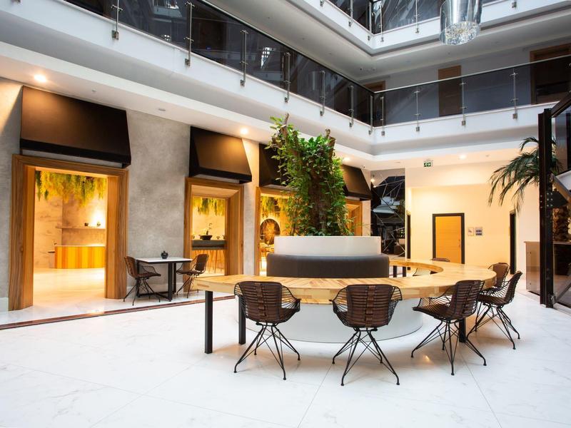 Modern hotel lobby with seating area, plants, and warm lighting in an open atrium space.