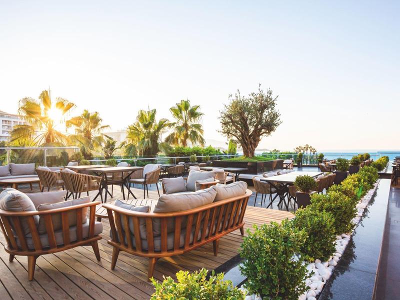Terrace with seating area, wooden chairs, and palm view at sunset at the hotel