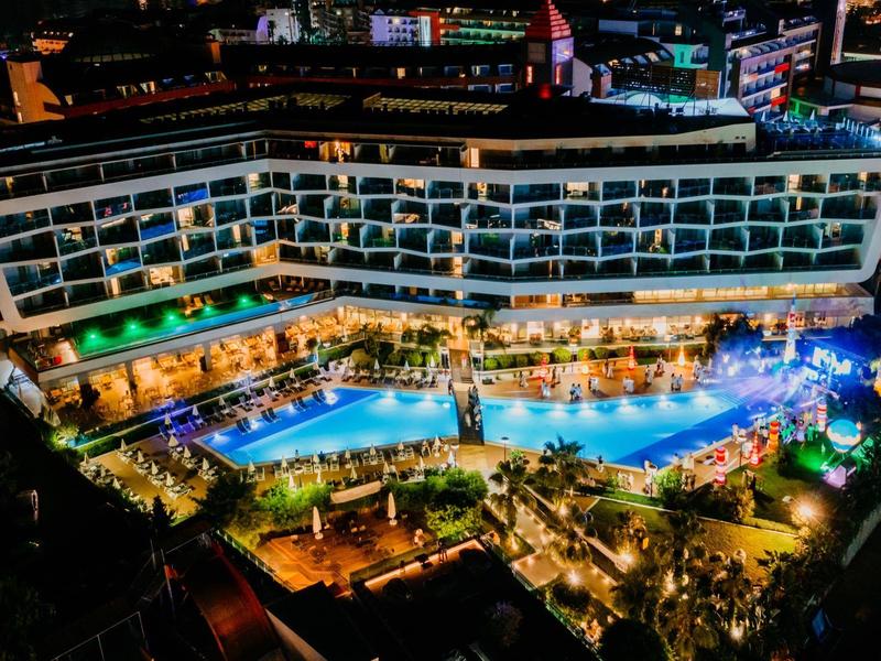 Illuminated hotel with large outdoor pool and surrounding greenery at night