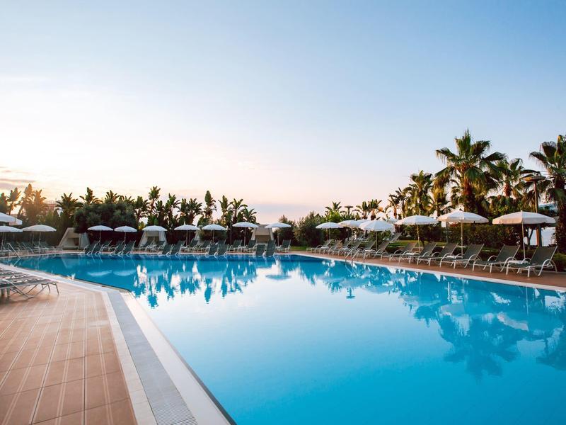 Outdoor pool at sunset surrounded by palm trees and lounge chairs with umbrellas.