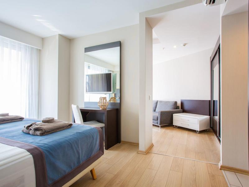 Bright hotel room with a bed, towels, mirror, and a living area with sofa and ottoman.