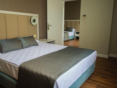 Moderní hotelový pokoj s manželskou postelí, šedým povlečením a dřevěnou podlahou.