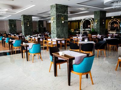 Prostorná moderní jídelna s modrými židlemi a dřevěnými stolky, světlá mramorová podlaha.