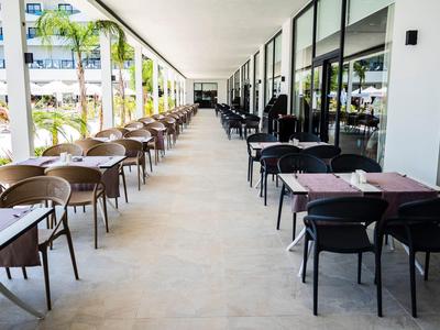 Hotelová restaurace s židlemi a stoly řazenými pod střechou na terase.