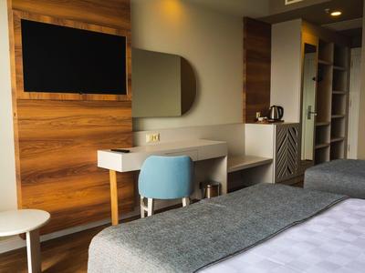 Moderní hotelový pokoj s dvěma postelemi, psacím stolem, modrým křeslem a dřevěnou dekorací.