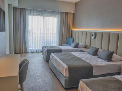 Moderní hotelový pokoj s velkými postelemi, křeslem a bílými závěsy.