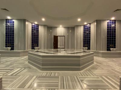 Prostorná turecká lázeň s bílým mramorem a jemným osvětlením.