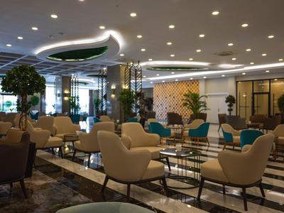 Moderní hotelový salonek s béžovými křesly, stoly, rostlinami a elegantním osvětlením.