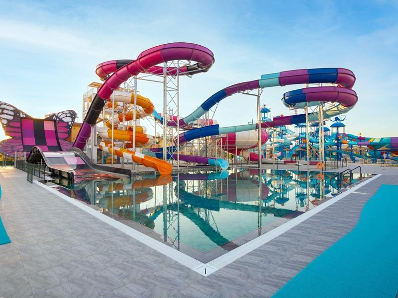 Vodní park s barevnými skluzavkami a bazénem pod jasnou oblohou.