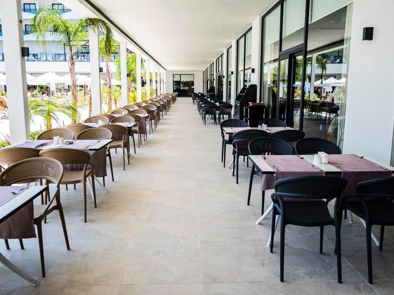 Hotelová restaurace s židlemi a stoly řazenými pod střechou na terase.