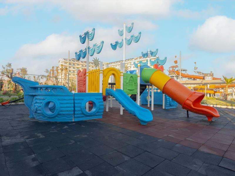 Barevné dětské hřiště ve tvaru lodě s modrými, červenými a žlutými skluzavkami.
