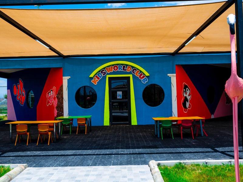 Barevná fasáda kavárny s venkovními stolky pod žlutou střechou.