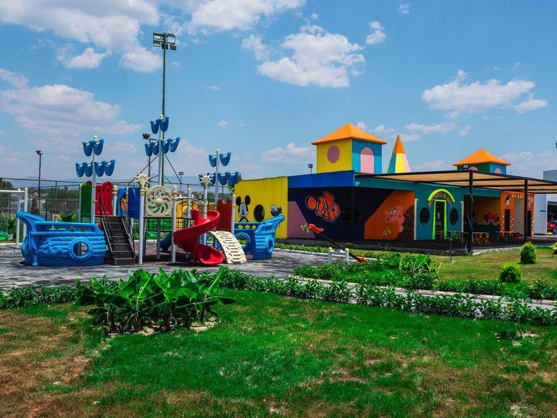 Barevné dětské hřiště u budovy pod částečně oblačnou modrou oblohou.