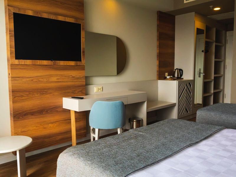 Moderní hotelový pokoj s dvěma postelemi, psacím stolem, modrým křeslem a dřevěnou dekorací.