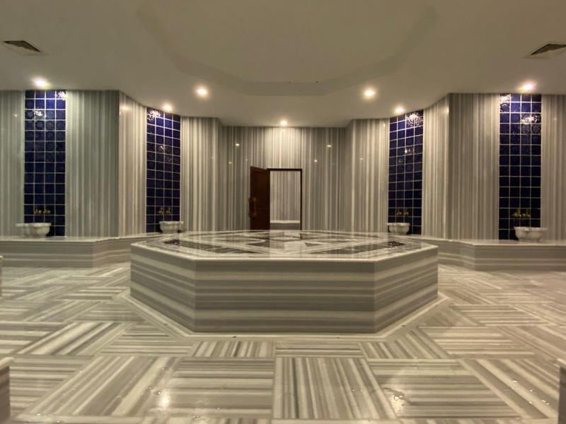 Prostorná turecká lázeň s bílým mramorem a jemným osvětlením.