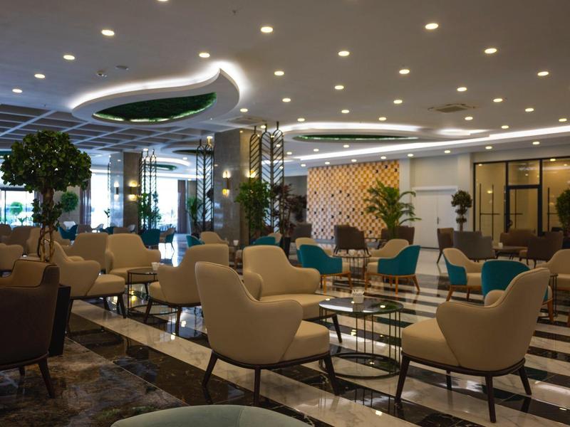 Moderní hotelový salonek s béžovými křesly, stoly, rostlinami a elegantním osvětlením.