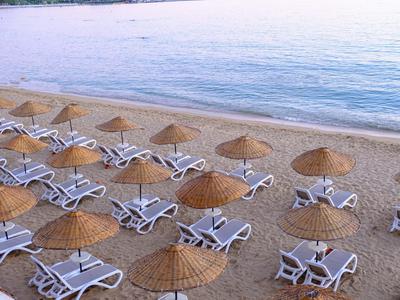 Prázdná lehátka se slámovými slunečníky na klidné písečné pláži u moře.