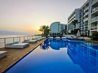 Piscina moderna de hotel con tumbonas y vista al mar al atardecer