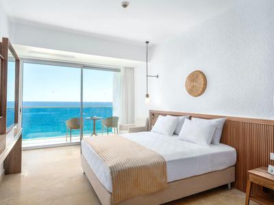 Licht hotelkamer met tweepersoonsbed, balkon en helder zeezicht.