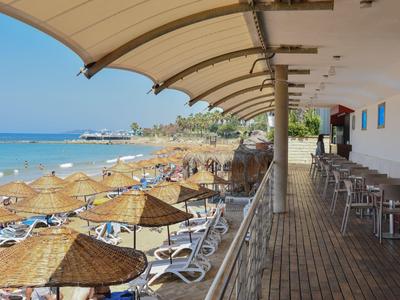 Zastřešená terasa s jídelními stoly na pláži s výhledem na moře a lehátka se střešními krytinami z trávy.